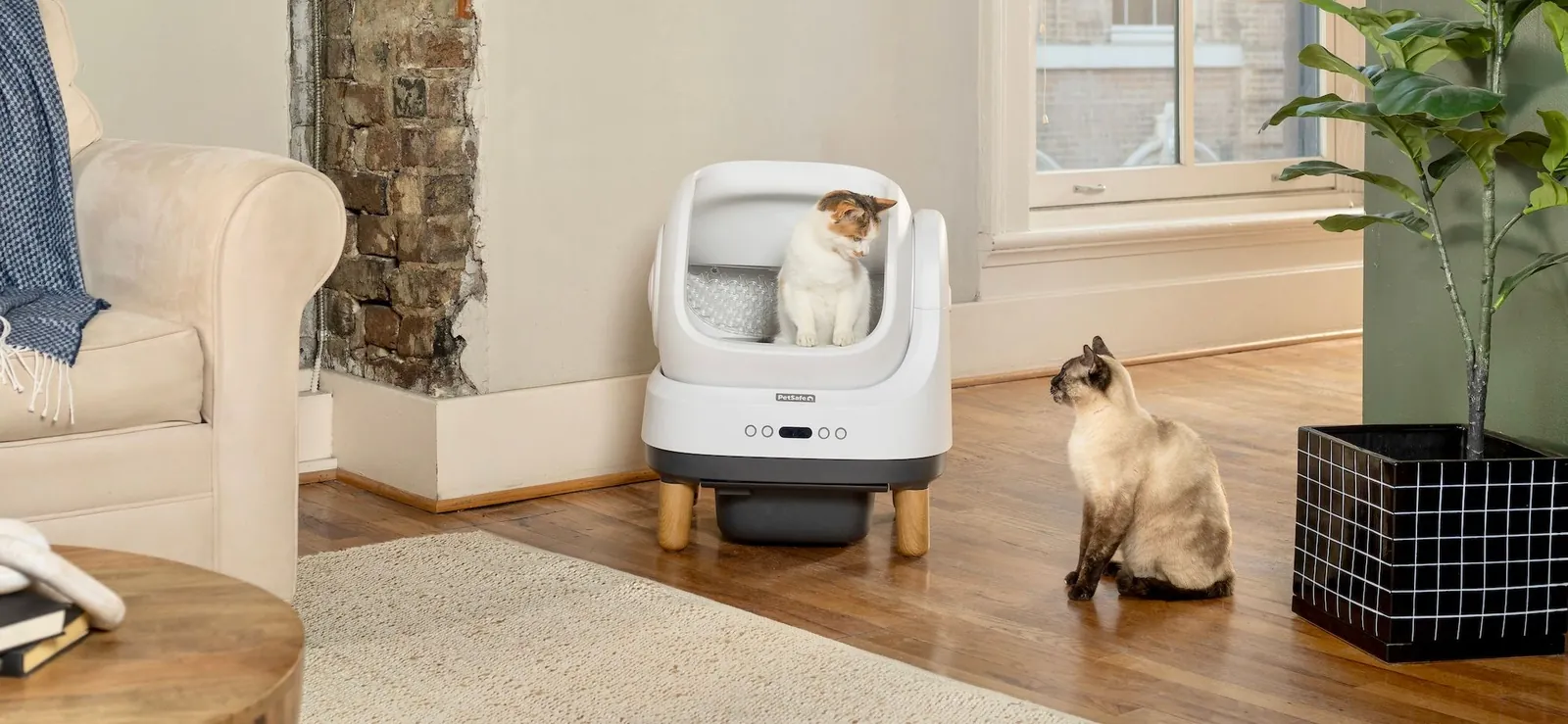 A durable litter box beside a torn plastic liner on a tiled floor.