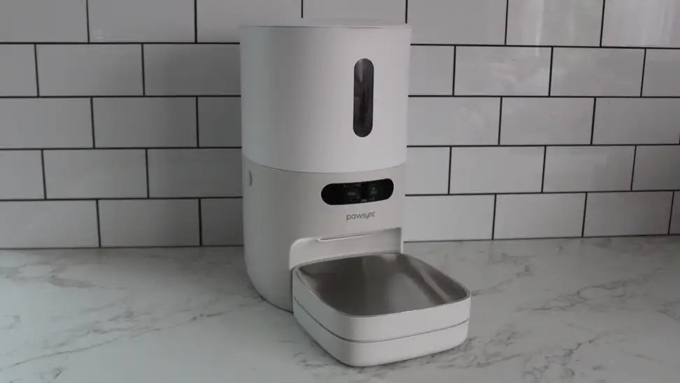 A modern smart pet feeder placed in a bright, clean living room setting.
